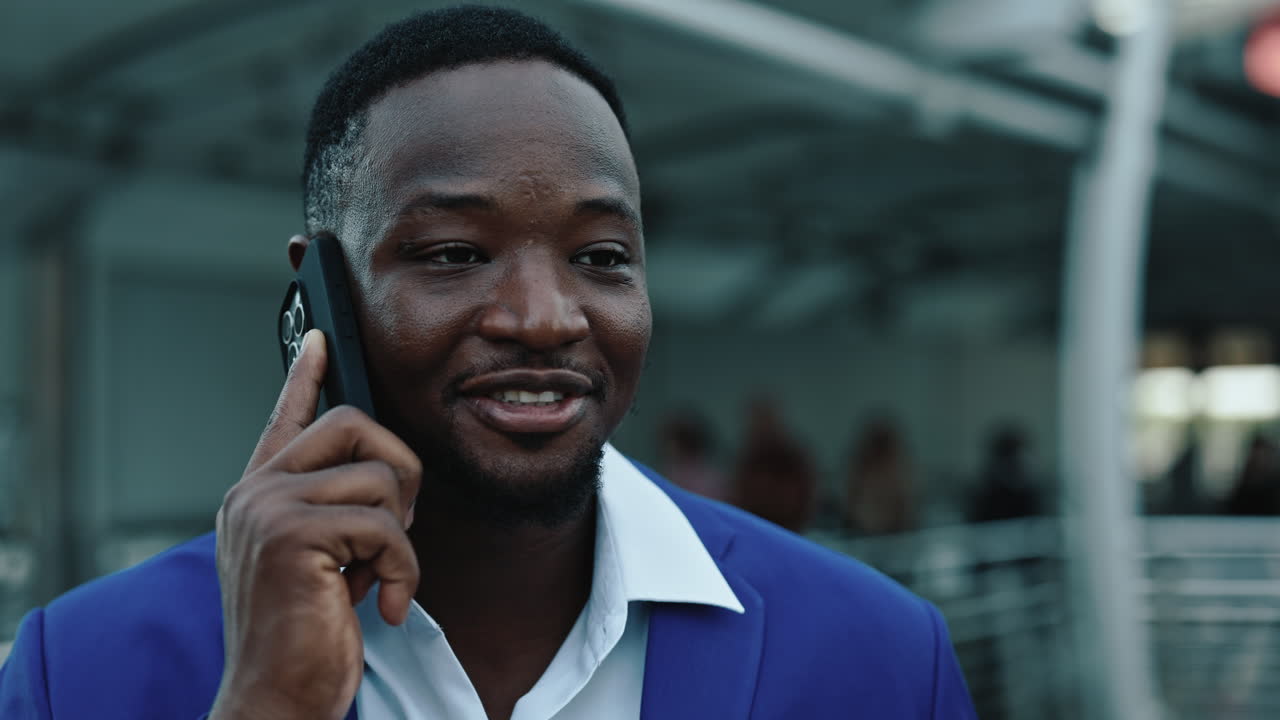 A Black man in a blue suit talks on his smartphone outdoors