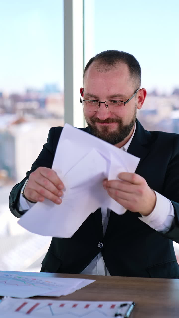 Depressed businessman sitting at desk. Bearded middle aged man in glasses feeling nervous at his workplace. Portrait of sad businessman in office. Vertical video