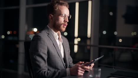 pleasant stylish man with a tablet on the background of the night city and drinks water