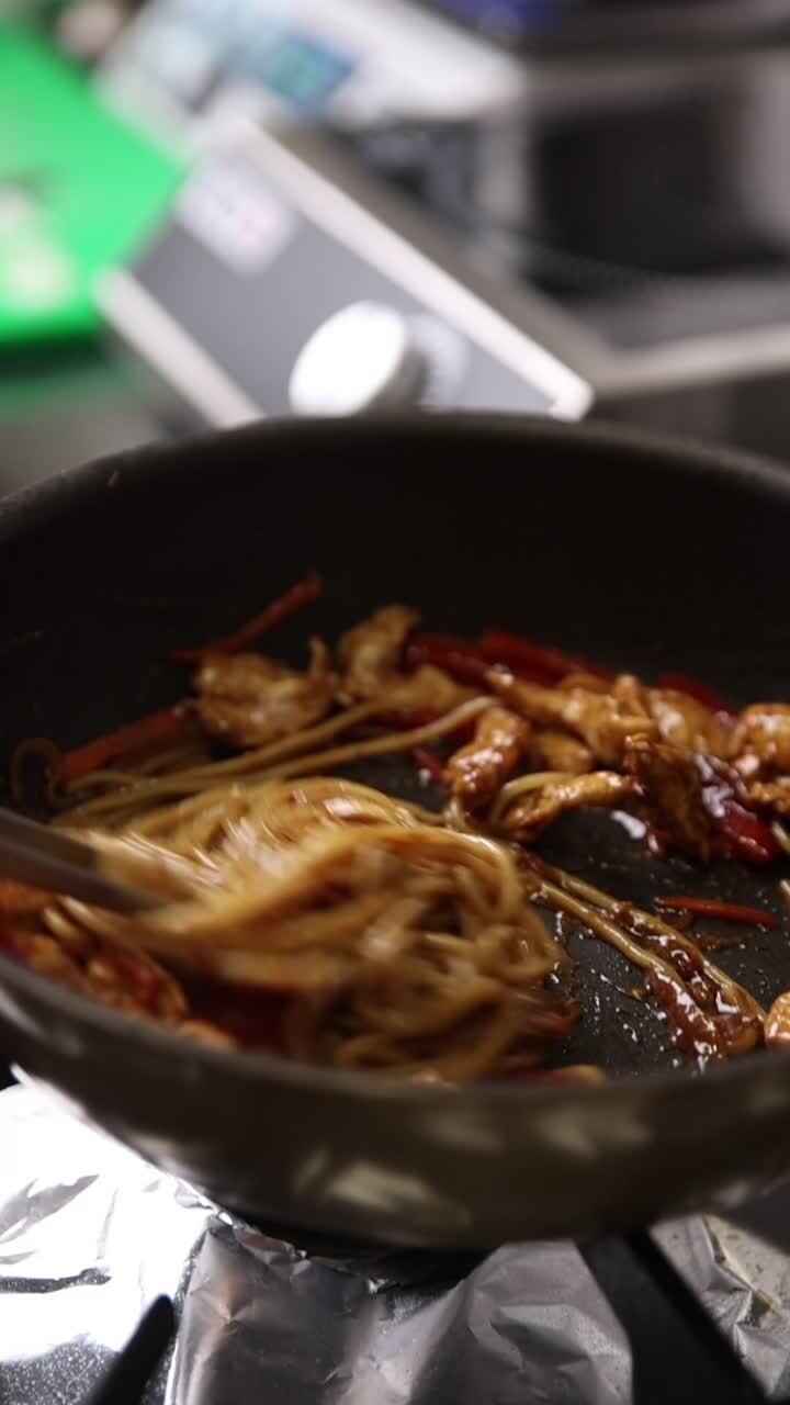 Chef che mescola noodles con pollo e verdure in una padella calda