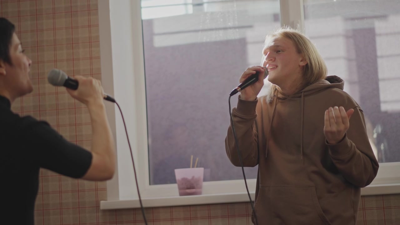 Singer practicing with vocal coach. Duet exchange in intimate rehearsal space, microphones raised, mentor gives feedback and encouragement, sunlight through window, playful energy and collaborative