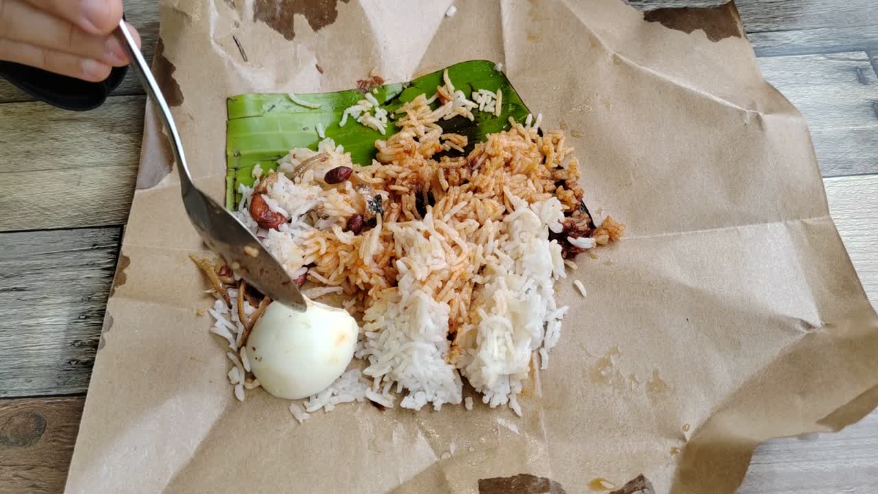 A woman enjoys nasi lemak bungkus, Malaysia's popular, quick breakfast. This simple meal, with egg and sambal, comes conveniently wrapped in paper for easy portability