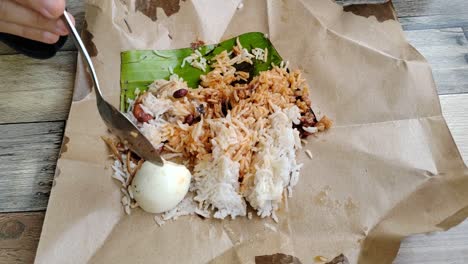 a woman enjoys nasi lemak bungkus, malaysia's popular, quick breakfast. this simple meal, with egg and sambal, comes conveniently wrapped in paper for easy portability