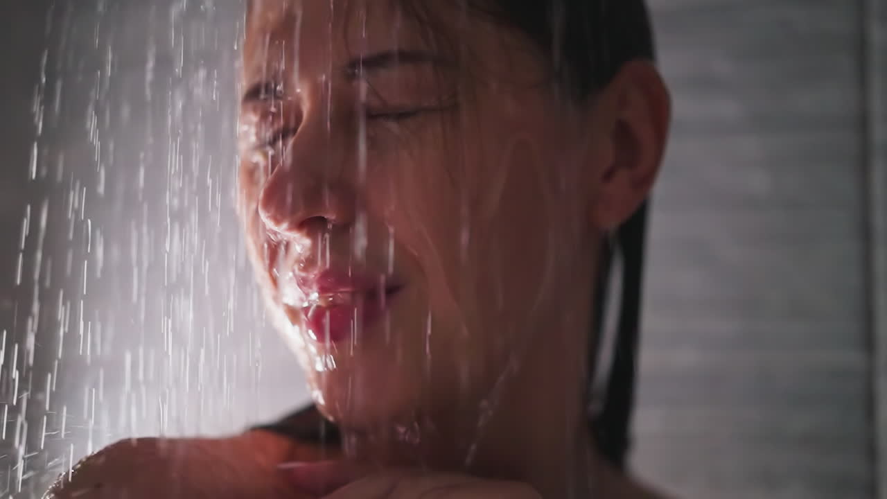 샤워 유 클로즈업에서 얼굴에 물방울이 떨어지는 긍정적 인 여성. 예쁜 여자는 가정 욕실에서 몸을 는 따뜻한 제트를 즐니다. 욕실에서 휴식을 취합니다.