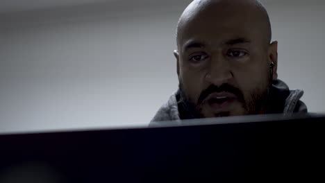 un hombre asiático calvo y guapo que parece severo mientras conversa con alguien en la pantalla del portátil