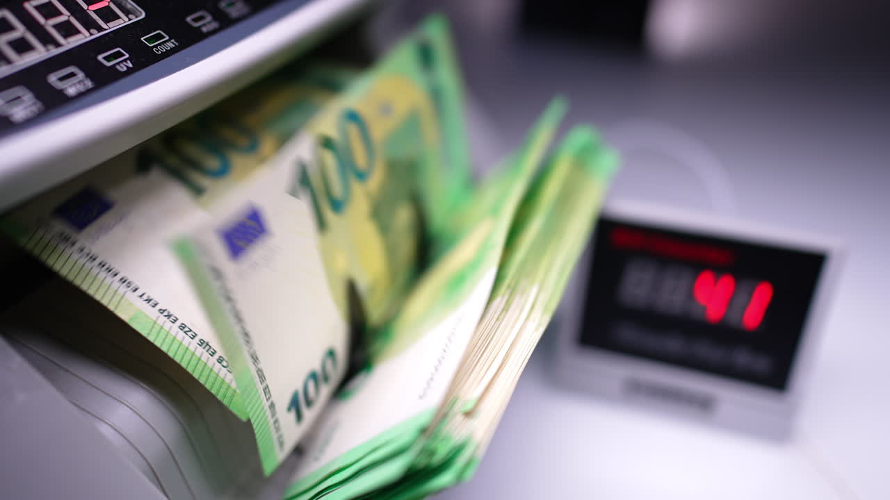 Blades of money counting machine rotate and one hundred euro bills appear. Display shows red changing numbers. Close up.