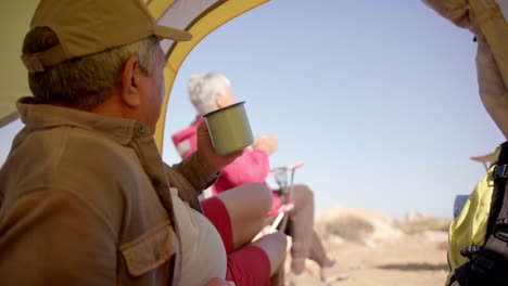 Feliz-Pareja-Birracial-De-Ancianos-Tumbada-En-Una-Tienda-De-Campaña-En-Las-Montañas-Y-Tomando-Café,-En-Cámara-Lenta