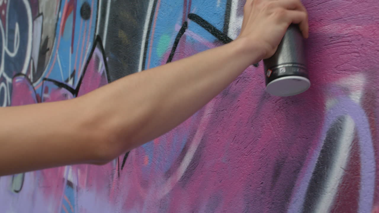 A man's arm and hand spraying paint graffiti on a wall in slow motion.