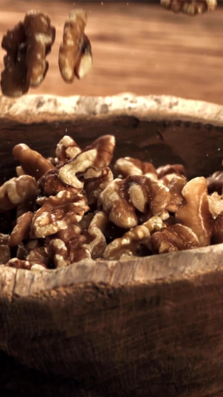 Walnuts Falling into a Rustic Wooden Bowl in Slow Motion