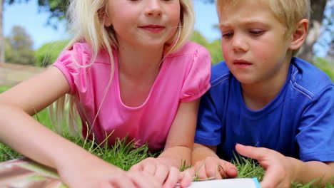 girl pointing to pages of a book as she reads to her brother