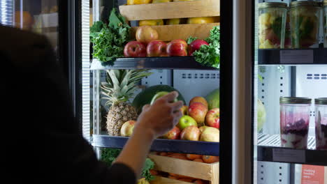 primer plano de la mano de una mujer abriendo la nevera y sacando fruta y cerrando la nevera