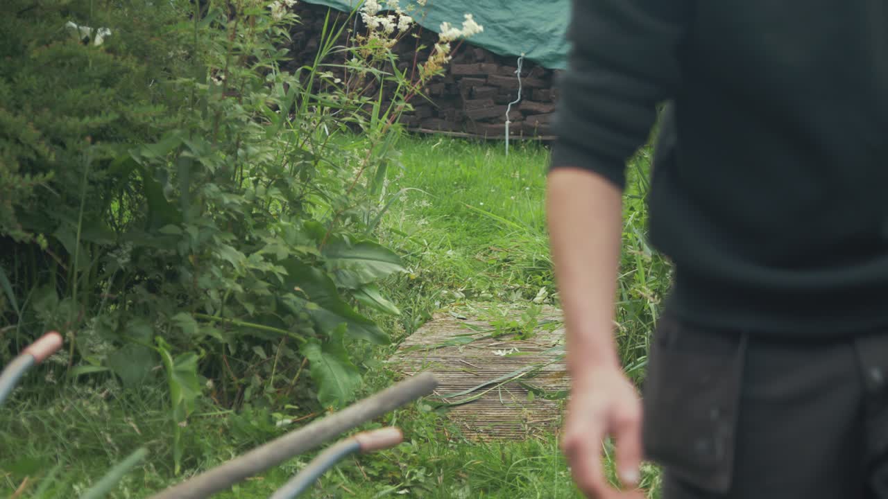 Young man walks over bridge with wheelbarrow after collecting garden clippings