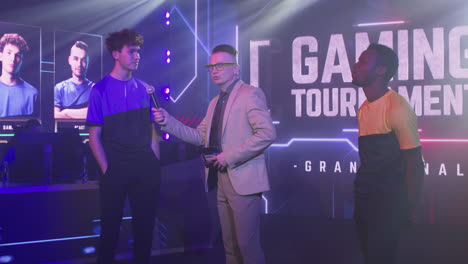 diverse gamers shaking hands after interview young man esportsman answering questions of announcer host then shaking hand of black rival and walking away at start of gaming competition