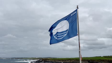 a blue flag with asos logo waves by a rocky coastline under a cloudy sky