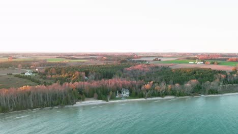 cinematic-aerial-of-a-charming-lakeside-cottage-sorounded-by-a-small-forest,-lake-and-beach