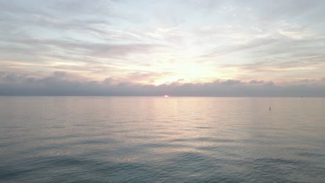 Vuelo-Bajo-Sobre-El-Agua-Hacia-El-Amanecer-Nublado-Rosa-En-El-Horizonte-Del-Océano