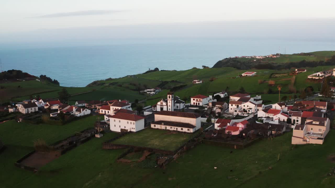 아조레스 섬의 푸른 화산 섬에서 해가 지는 동안 오래된 교회와 작은 유럽 마을의 순환 드론 영상