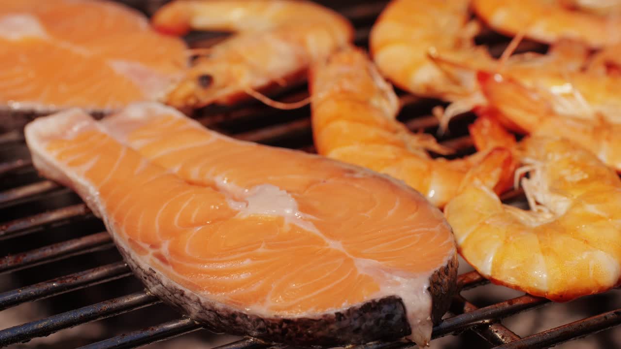 Chef cooking shrimps with oil and spices on grill close-up. Prawns on fire throwing them on pan. Dorado and salmon fish steak on frying grill. Restaurant Food concept. Sea food barbecue.