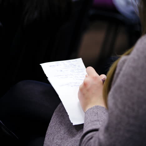 young female is writing on a sheet of paper. woman is sitting in a conference hall and notes some information. close-up.