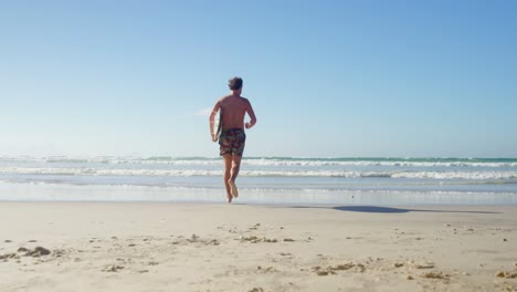 hombre corriendo con una tabla de surf en la playa en un día soleado