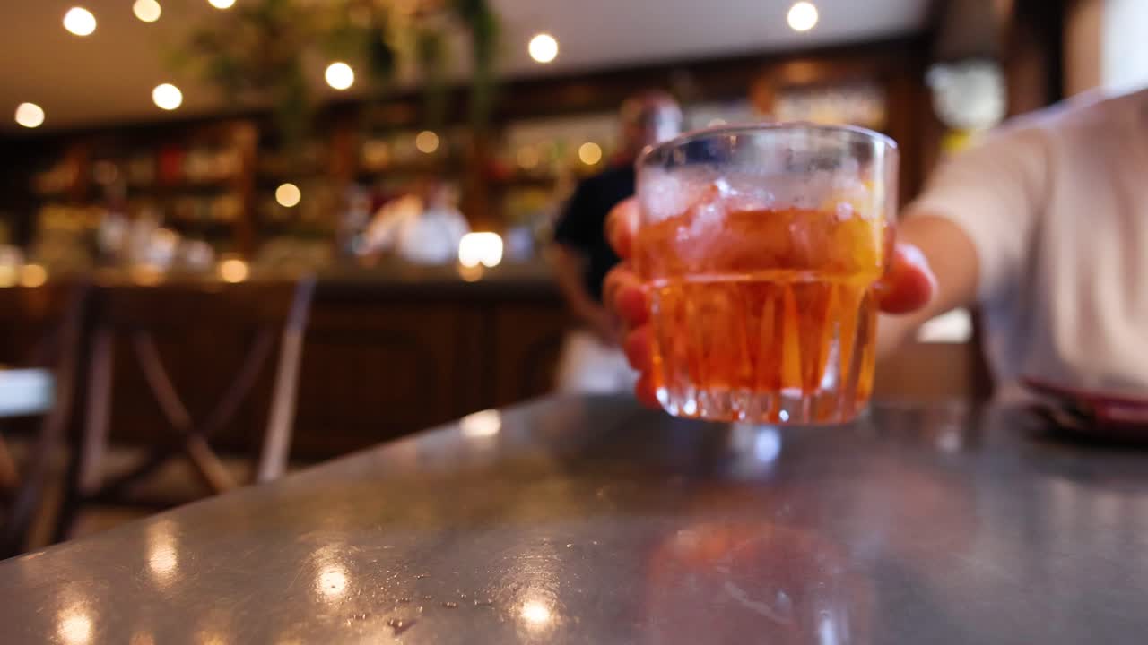 Mano che afferra un Aperol Spritz in un bar