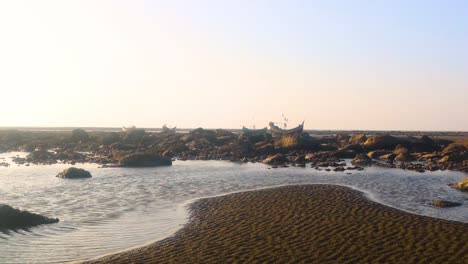 Pozas-De-Marea-En-Marea-Baja-En-Una-Costa-Rocosa-Con-Barcos-De-Pesca-En-El-Fondo