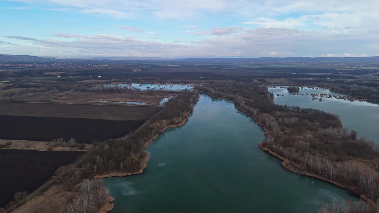 En Miskolc, Hungría, el lago Csorba aparece como un tranquilo cuerpo de agua dulce bordeado por humedales, prados y colinas boscosas bajo un cielo nublado en una vista aérea