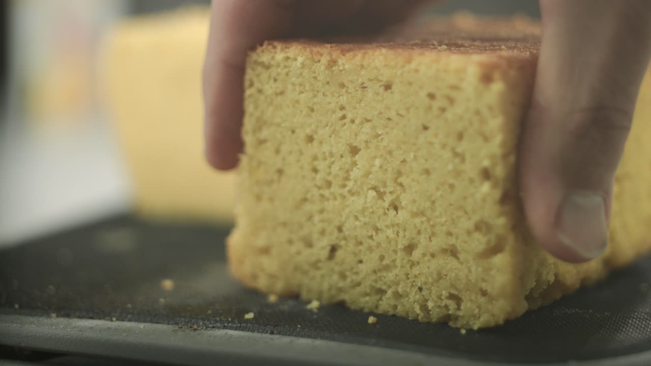 Uno chef che testa la consistenza di un pan di Spagna vegano appena sfornato, con un pezzo di torta affettato nel punto focale