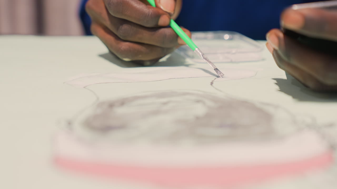 Black hands painting portrait sketch on table, closeup view of artist inking fine lines with green pencil, soft studio light, concentrated process, portrait commission, illustrative study