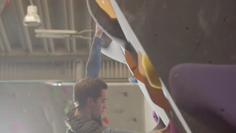 low angle shot of a strong male athlete climbing artificial rock wall in bouldering gym