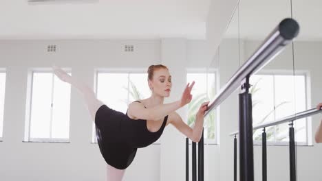 caucasian female ballet dancer stretching up by the mirror in a bright studio