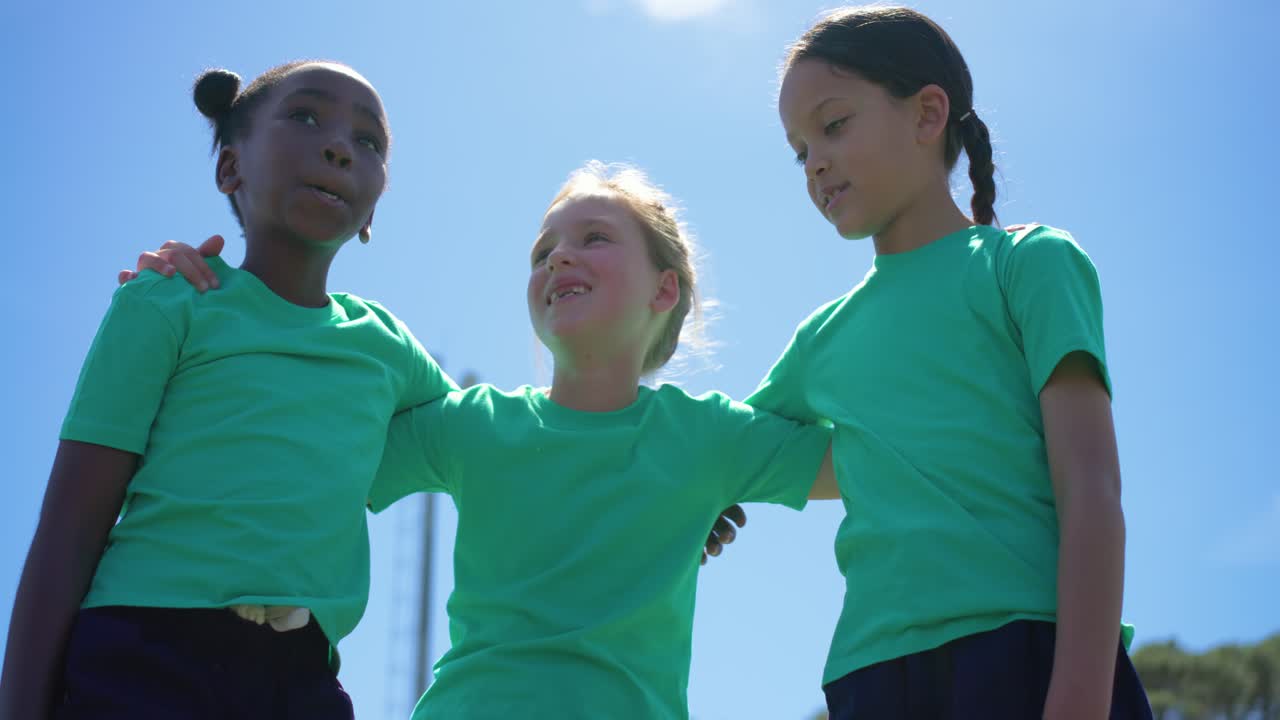 Three female children pre-game huddling stacking palms and raising arms on field wearing green tees