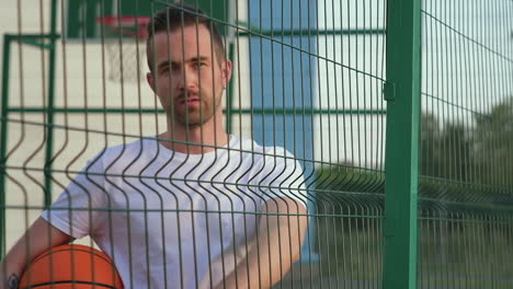 man pointing through a fence at a basketball court