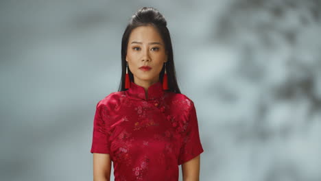 portrait shot of asian young cheerful woman in red traditional clothes looking with serious expression at camera