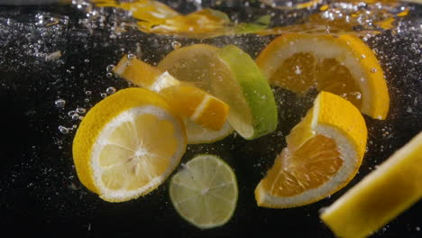 muchas frutas cítricas en rodajas en cámara lenta salpican en agua con burbujas de bebida