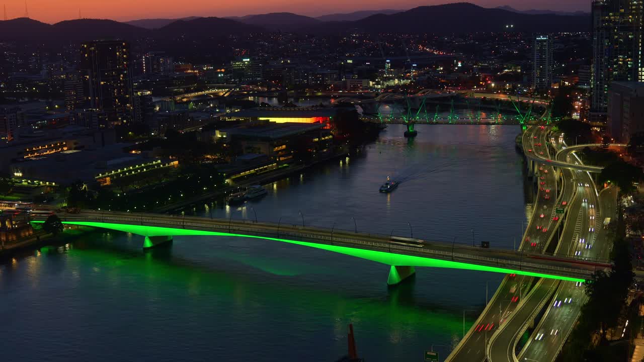 Beautiful dusk to night time-lapse shot of the vibrant Brisbane city, busy riverside motorway traffics, buses crossing on illuminated Victoria bridge and ferries cruising on the river.