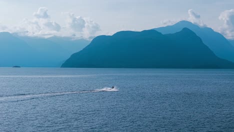 an aerial drone shot of a jetski on the blue waters of lions bay sailing towards anvil island under a clear blue sky