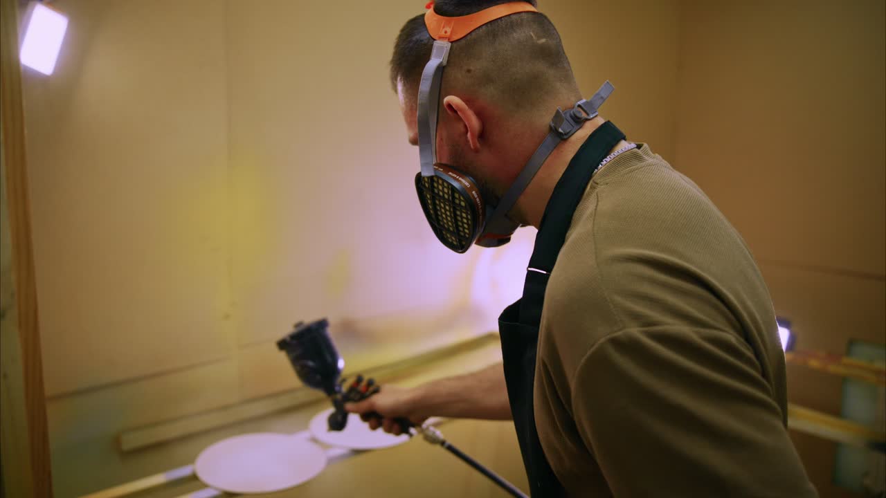 Man in Respirator Mask Spray Painting Wooden Pieces in Workshop