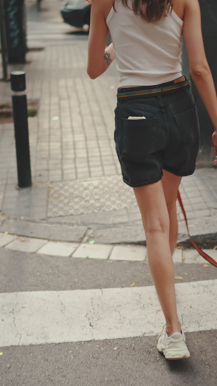 A woman walking a black dog on a sidewalk
