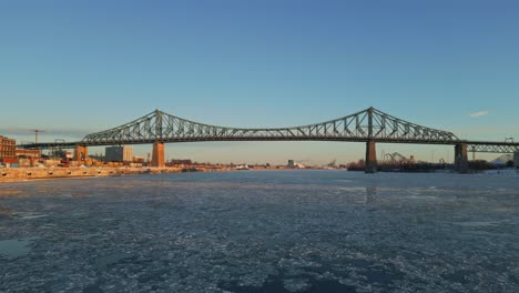 aerial view of montreal’s iconic steel bridge spanning over the frozen st. lawrence river, north america, quebec, montreal, canada.