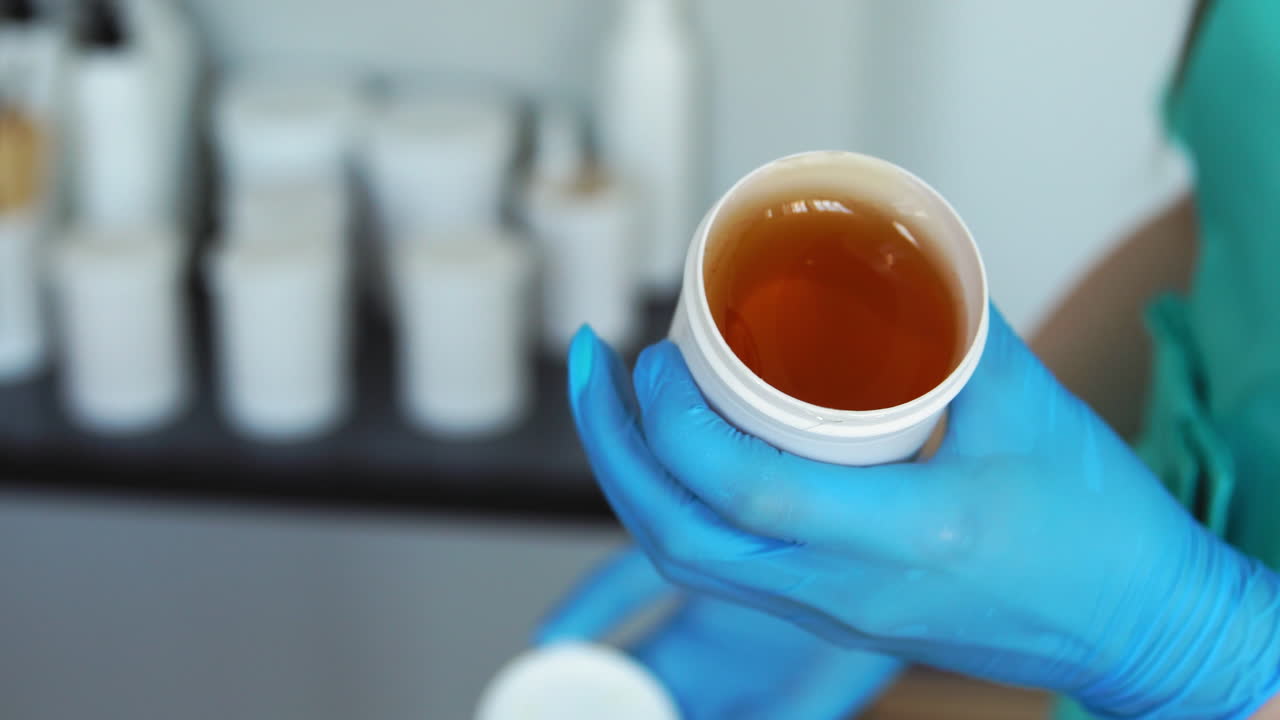 Primo piano di mani con guanti di gomma che aprono un barattolo di zucchero per la depilazione con il sugaring.