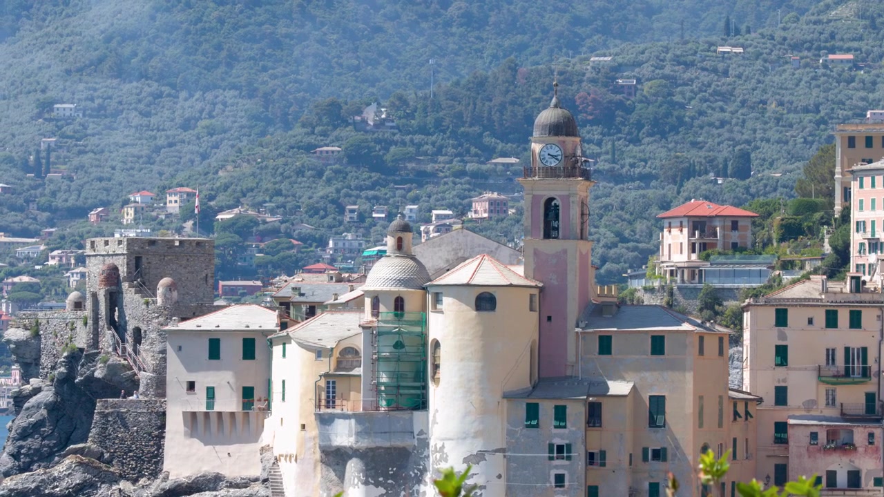 Inquadratura ampia statica di una storica torre dell'orologio e di edifici colorati lungo la costa italiana.