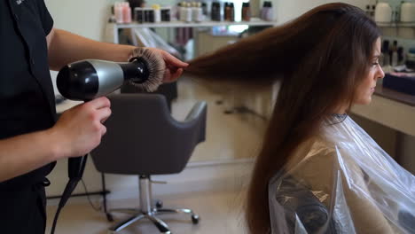 hair stylist blow-drying client's long hair at a salon
