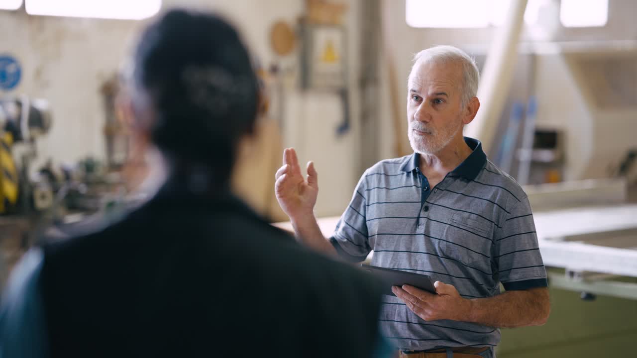 Senior Man Discussing Work in a Workshop While Holding a Tablet