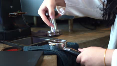 female barista tamping a portafilter for even extraction of espresso brewing at cafe setting