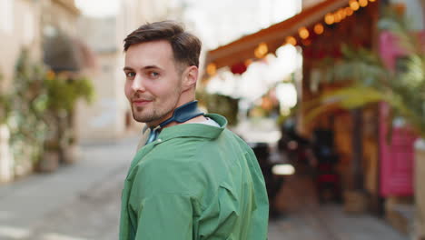 Portrait-of-happy-man-stands-turns-around-smiling-friendly-glad-expression-looking-at-camera-street