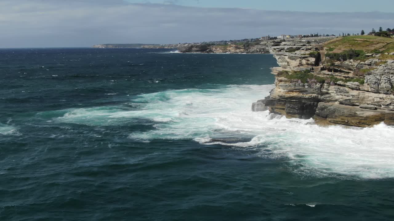 Flying around Jagged coastline near Bondi beach with stormy waves crashing on cliff in Australia