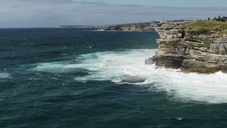 Flying-around-Jagged-coastline-near-Bondi-beach-with-stormy-waves-crashing-on-cliff-in-Australia