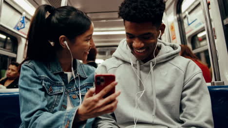 young people sharing a smartphone and earphones on a subway train