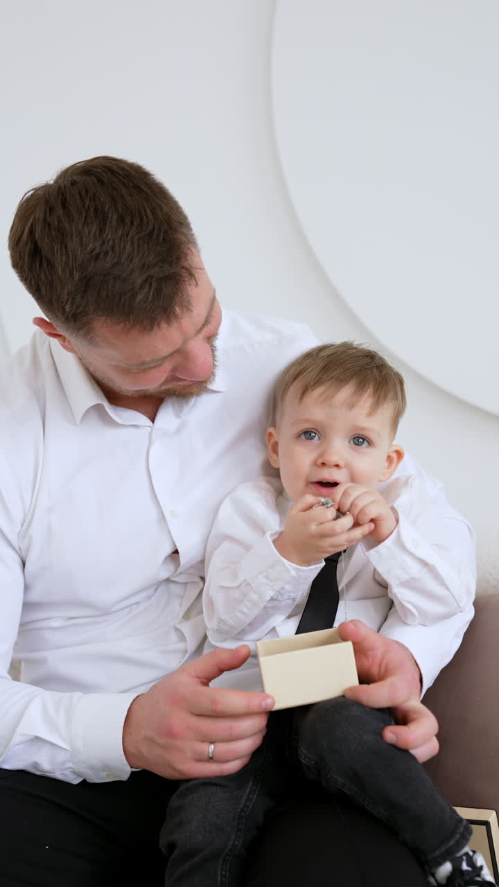 Bearded Caucasian man in white shirt holds a baby boy. Cute kid pulls the jewelry from the box. Vertical video.